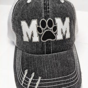 May include: Black and white trucker hat with a white "MOM" with a black paw print in the center, all embellished with rhinestones.