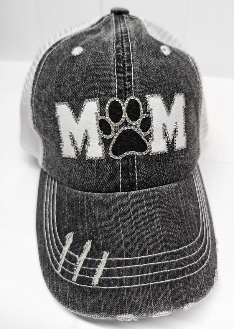 May include: Black and white trucker hat with a white "MOM" with a black paw print in the center, all embellished with rhinestones.