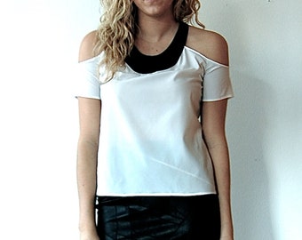 May include: A woman wearing a white off-the-shoulder top with a black collar and a black leather mini skirt. She is wearing black heels.