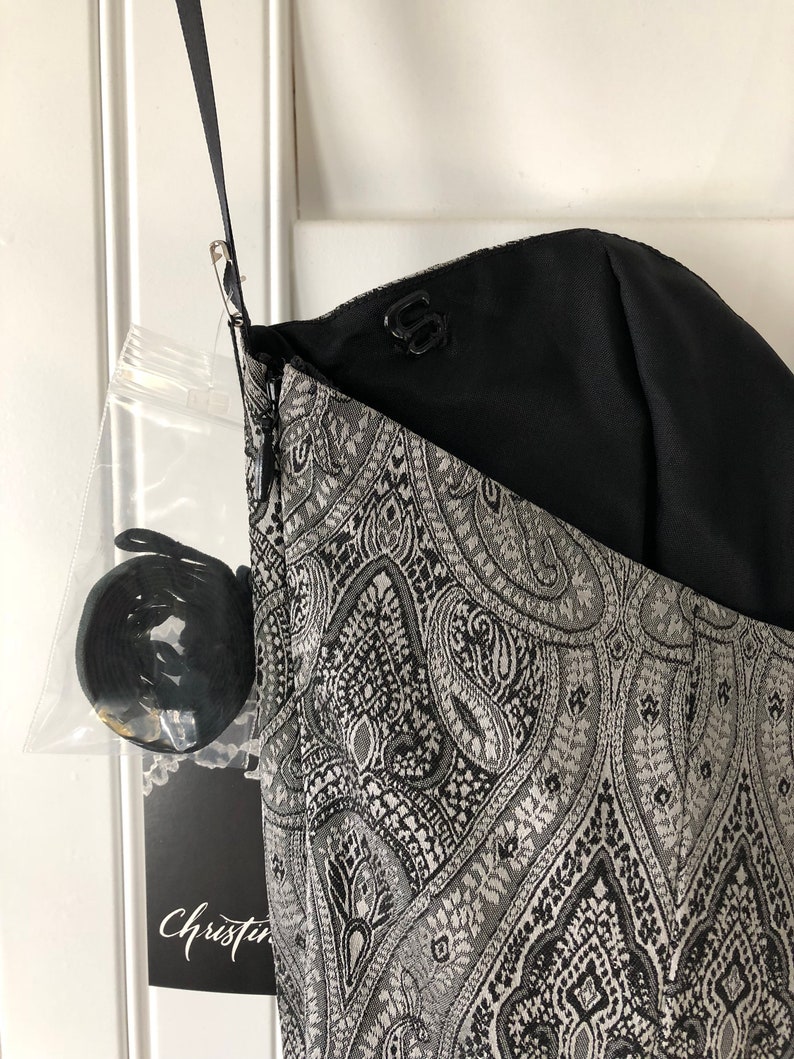May include: A black and silver paisley patterned dress with a black lining and a zip closure. The dress has a label that says "Christine".