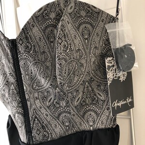 May include: A black strapless dress with a silver and black paisley print bodice and a black skirt. The dress has a zip fastening at the back and a tag that reads "Christina Kishi".