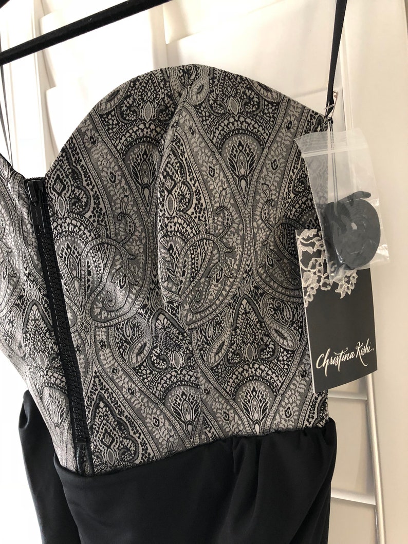 May include: A black strapless dress with a silver and black paisley print bodice and a black skirt. The dress has a zip fastening at the back and a tag that reads "Christina Kishi".
