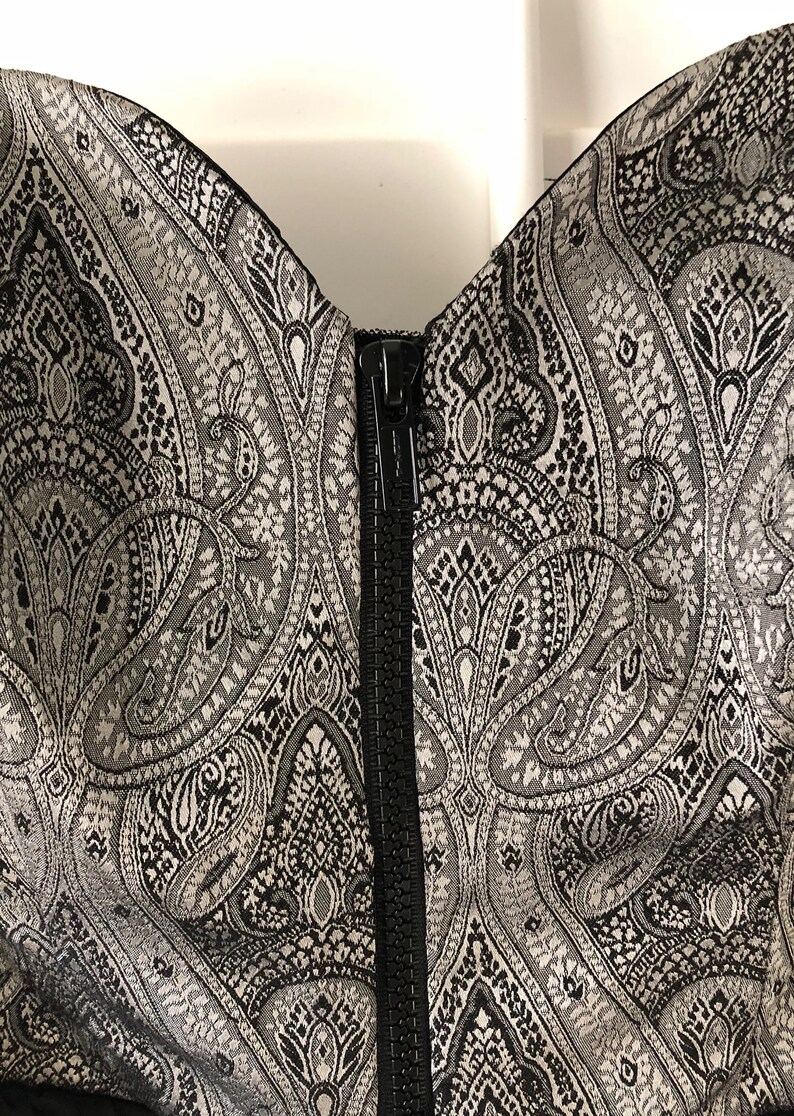 May include: A black and silver strapless dress with a paisley pattern and a black zip at the back.