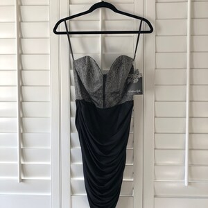 May include: A black and silver strapless dress with a fitted bodice and a ruched skirt. The bodice has a paisley pattern and the skirt is made of a stretchy fabric. The dress has a tag that says "Christian Audigier".