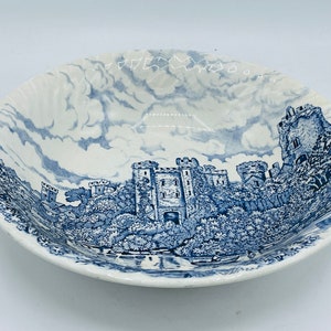 May include: A white ceramic bowl with a blue and white design of a castle and trees. The bowl has a scalloped edge.