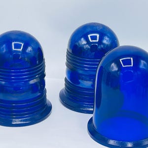 May include: Three vintage blue glass bell-shaped objects. The objects have a rounded top and a flared base. The two objects on the left have horizontal ridges. The objects are a deep, saturated blue color and appear to be made of glass.