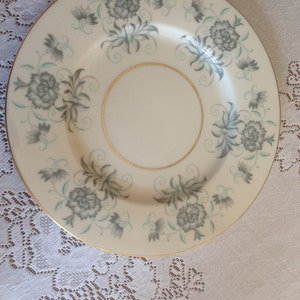 May include: A white ceramic plate with a gold rim and a floral design in shades of gray and green.
