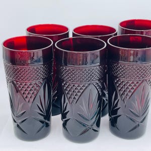 May include: Set of six ruby red drinking glasses. Each glass features a diamond and leaf pattern on the lower half and a smooth rim. The glasses are cylindrical and appear to be made of glass.