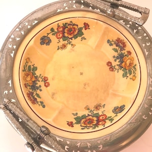 May include: A vintage silver-plated serving dish with a floral design. The dish has a scalloped edge and two handles. The floral design features yellow, red, and blue flowers on a cream background.