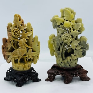 May include: Two hand-carved jade sculptures on wooden bases. The sculpture on the left features a bird and floral designs. The sculpture on the right features a floral design.