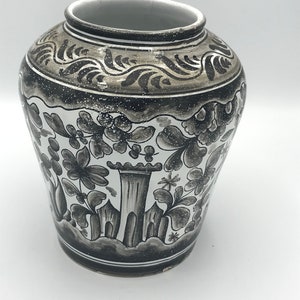 May include: A white ceramic vase with black and gray floral designs. The vase has a rounded body and a wide mouth.