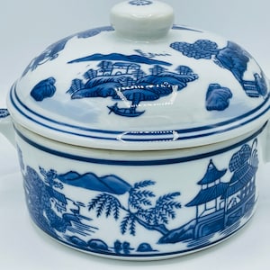 May include: A white porcelain serving dish with a blue and white floral design. The dish has a lid and two handles.