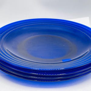 May include: A stack of four blue glass dinner plates. The plates have a slightly rippled edge.