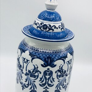 May include: A white ceramic jar with a blue and white floral design. The jar has a lid with a knob on top.
