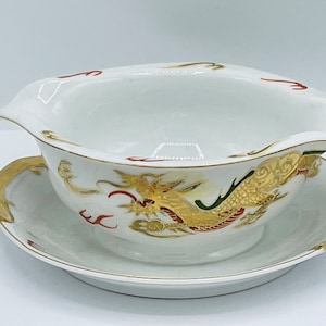 May include: White porcelain gravy boat with a gold and red dragon design. The boat has a matching saucer with a gold rim.