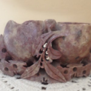 May include: A hand-carved stone incense burner with a floral design. The burner is made of reddish-brown stone and has two small bowls for incense.
