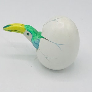 May include: A ceramic toucan figurine with a yellow beak, green and blue feathers, and a white egg shell with blue cracks.