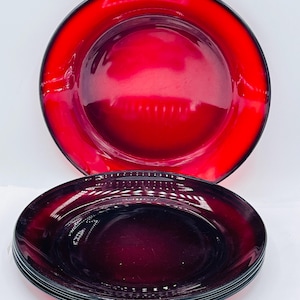 May include: A stack of red glass plates with a black rim. The plates are a deep red color and have a glossy finish. One plate is stacked on top of the others. The plates are round and have a slightly raised edge.