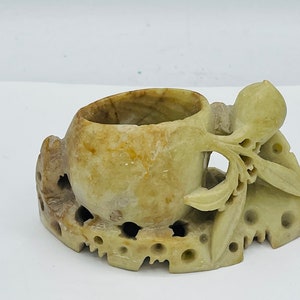 May include: A carved stone incense burner with a round, hollowed-out top and intricate floral designs. The base is also carved with a floral motif and has several open holes.