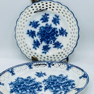 May include: Two decorative porcelain plates with a blue and white floral design. The plates have a scalloped edge and a delicate openwork pattern.