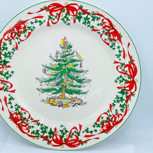 May include: A white ceramic Christmas plate with a green Christmas tree and red bows around the edge.