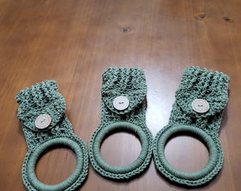 May include: Three green crocheted towel rings with a button on each. The rings are made with a textured stitch and have a pocket on the back.