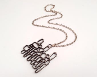 Peut inclure: Un collier pendentif en métal argenté présentant un design abstrait ajouré composé de boucles circulaires et rectangulaires arrondies interconnectées. Le pendentif est suspendu à une chaîne en métal argenté assortie à maillons ovales.