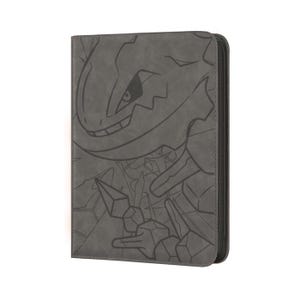 May include: A dark gray rectangular trading card binder featuring a debossed graphic of a stylized creature with sharp features and geometric shapes on the front cover. The binder has a smooth, matte finish and a vertical zipper closure along the side.