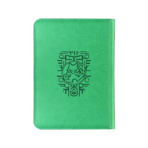 May include: A bright green rectangular notebook with rounded corners. The cover features a dark green embossed graphic of a stylized cat-like creature centered within a geometric frame, accompanied by abstract symbols above and below the design.
