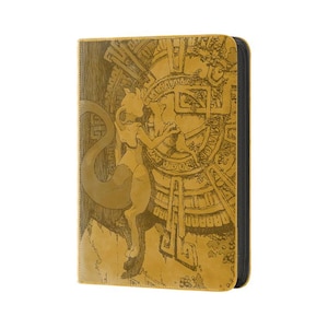 May include: A rectangular yellow binder featuring a detailed dark brown engraved illustration of the character Mewtwo standing before a large circular stone-like structure with intricate geometric patterns and a black zippered edge.