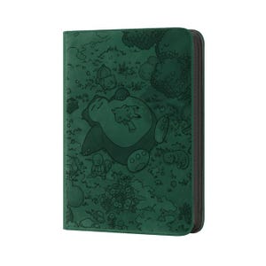 May include: A dark green card binder featuring an embossed design of a sleeping Snorlax with Pikachu and other Pok&eacute;mon characters in a forest scene. The binder has a black zipper closure and a textured surface.