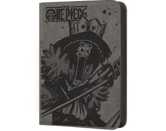 May include: A gray zippered wallet featuring a black illustration of a character from the anime series One Piece. The One Piece logo is at the top. The character is depicted with a crown and a musical instrument.