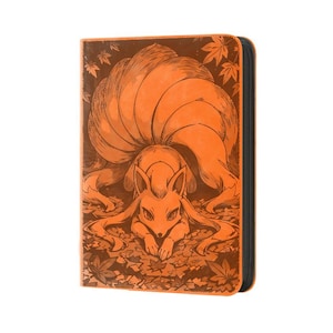 May include: An orange card binder featuring a stylized illustration of a fox with multiple tails, surrounded by autumn leaves. The fox is depicted in a crouching position. The binder has a black zipper and trim.