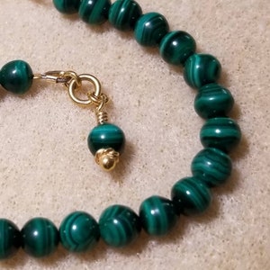 May include: A green malachite beaded bracelet with a gold clasp and a small malachite charm.