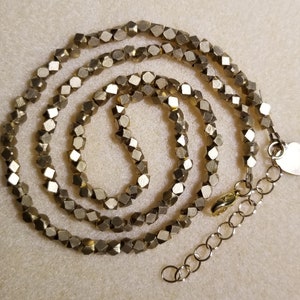 May include: A gold necklace made of small, faceted beads. The necklace is layered and has a heart-shaped clasp.