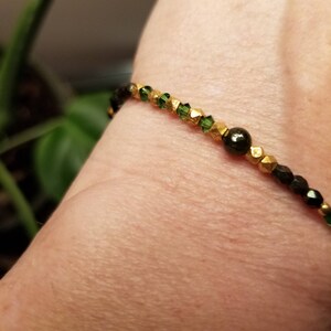Puede incluir: Un brazalete de cuentas verdes y doradas con una cuenta negra en el centro.