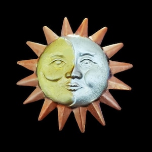 May include: A ceramic sun with a face split in half, one side painted gold and the other silver. The sun has a copper-colored border and 16 points.