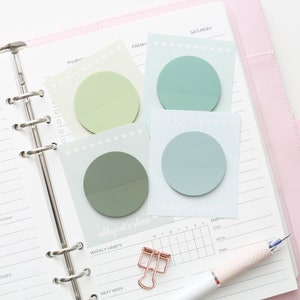 May include: Four pastel green and blue circle stickers with white hearts around the edges. The stickers are on a white planner page with the words "Thursday", "Friday", "Saturday", and "allycat's shop" written on them.