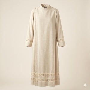 May include: A long-sleeved beige dress featuring a high neckline with button closures at the shoulder. The garment includes intricate white lace trim detailing around the cuffs and a horizontal lace band near the bottom hemline.