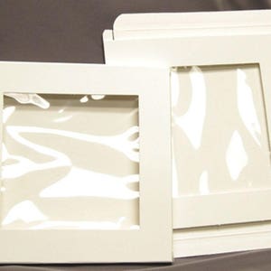 May include: Two white cardboard boxes with clear plastic windows. The boxes are designed to display and protect items.