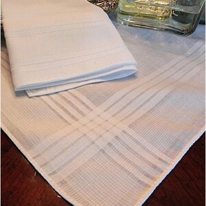 May include: A white cotton handkerchief with a delicate, woven pattern. The handkerchief is folded in half and has a smooth, soft texture.