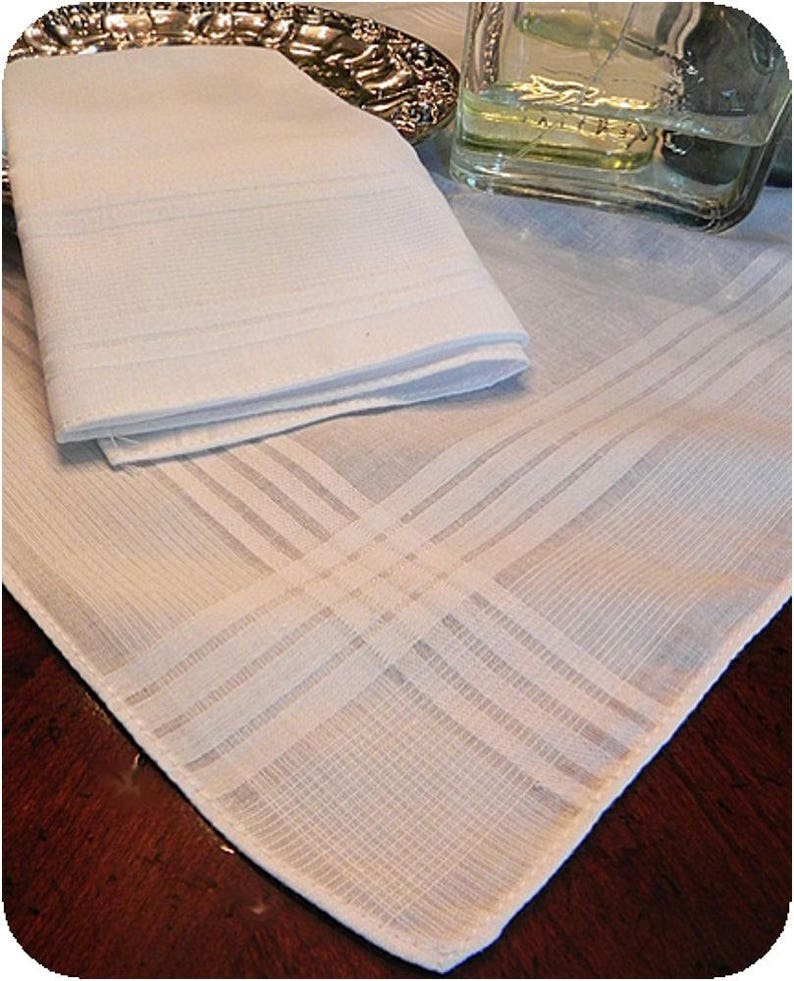May include: A white cotton handkerchief with a delicate, woven pattern. The handkerchief is folded in half and has a smooth, soft texture.
