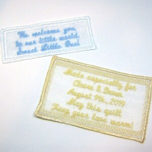 May include: Two white fabric labels with gold embroidered text. The top label says "We welcome you to our little world. Sweet Little One!" The bottom label says "Made especially for Claire & Devan August 9th, 2019 May this quilt keep your love warm!"