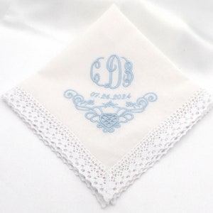 May include: White handkerchief with a blue embroidered monogram and the date "07.26.2024". The handkerchief has a white lace border.