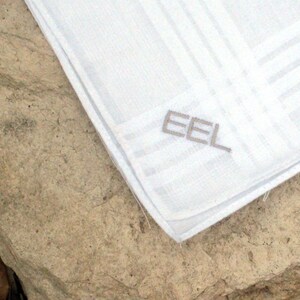 May include: White linen handkerchief with a gray embroidered "EEL" logo.