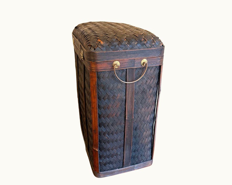 May include: A rectangular, dark brown woven bamboo storage basket with a hinged lid. The basket features brass handles and trim. The woven pattern creates a textured surface. The basket is designed for storage.