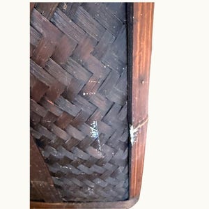 May include: Close-up of a dark brown woven basket with a rectangular shape. The basket's design features a diagonal weave pattern. The edges are framed with a darker wood, adding contrast to the overall aesthetic.