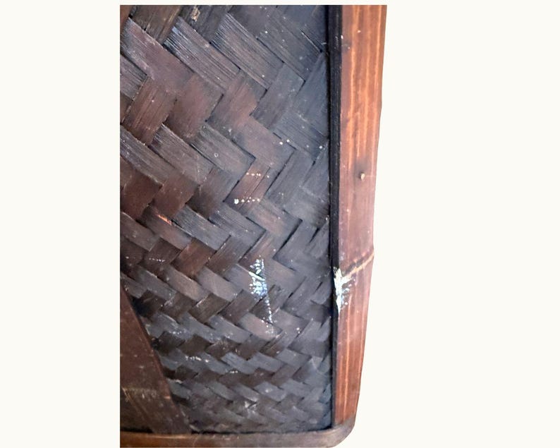 May include: Close-up of a dark brown woven basket with a rectangular shape. The basket's design features a diagonal weave pattern. The edges are framed with a darker wood, adding contrast to the overall aesthetic.