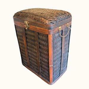 May include: A rectangular, dark brown woven bamboo storage chest with a hinged lid. The chest features a woven pattern, wooden trim, metal hardware, and a handle. The chest is designed for storage and organization.