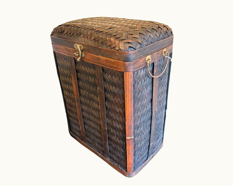 May include: A rectangular, dark brown woven bamboo storage chest with a hinged lid. The chest features a woven pattern, wooden trim, metal hardware, and a handle. The chest is designed for storage and organization.